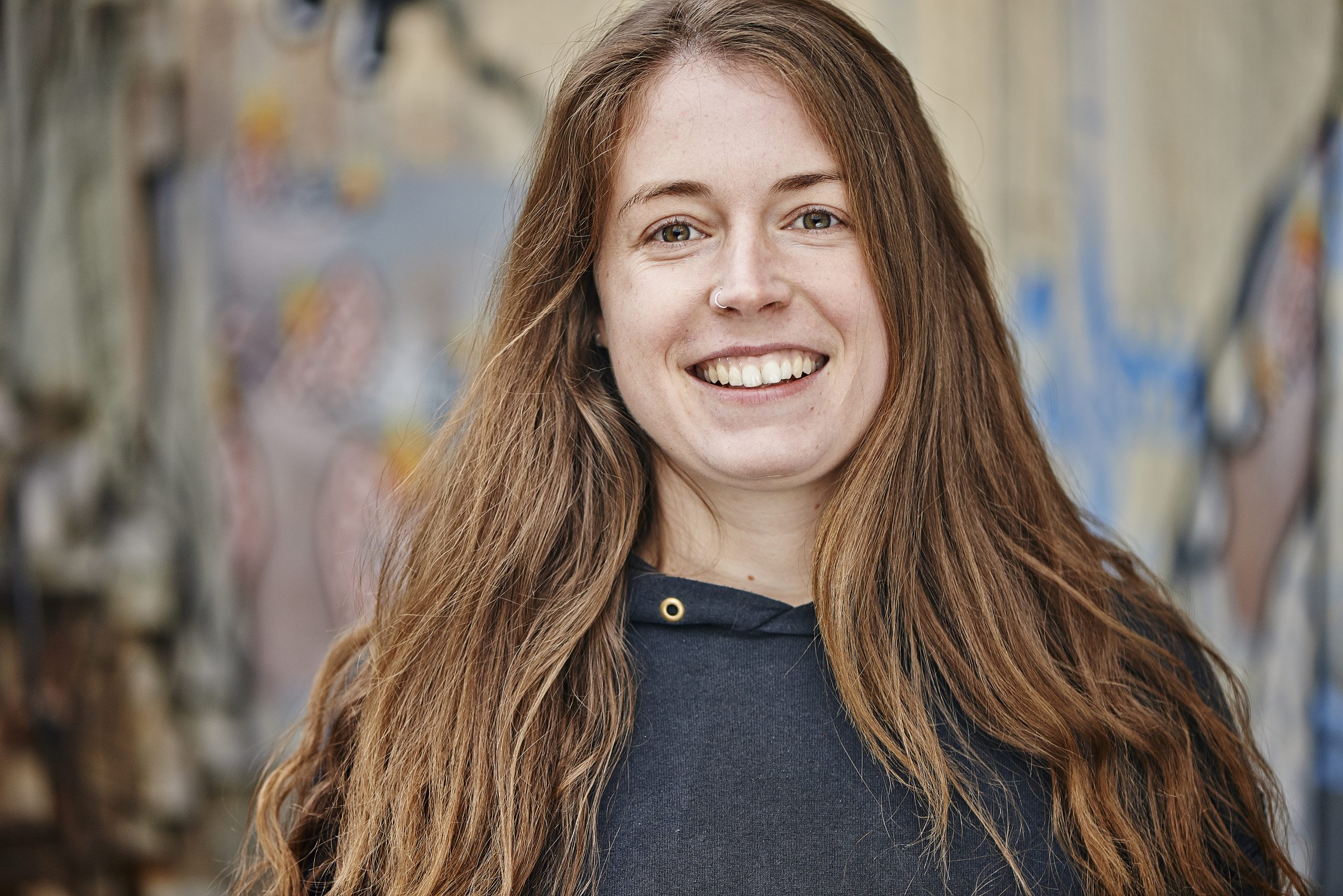 Portraitfoto einer jungen Frau mit braunen langen Haaren und einem offenen, freundlichem Lachen.