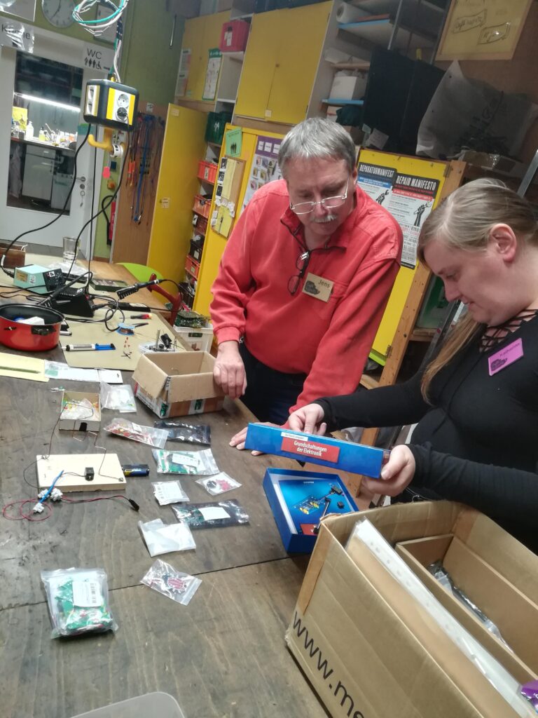 Zwei Personen stehen an der Werkbank und haben vor sich unterschiedliche L&ouml;tmaterialien.