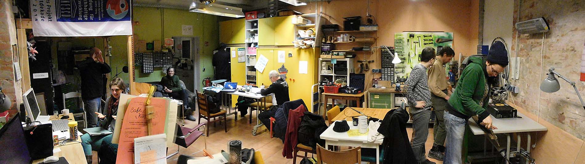 Mehrere Personen stehen in einem bunten Raum und widmen sich ihren Reparatur-Projekten.