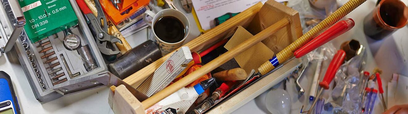 Auf einem Tisch sind mehrere Werkezuge verteilt. Dazwischen stehen zwei Kaffee Tassen. Eine Werkzeug-Kiste aus Holz steht in der Mitte.