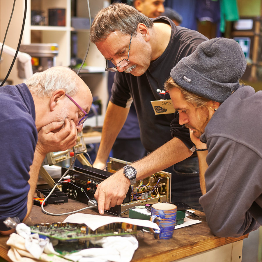 Drei Menschen sind über einen Receiver gebeugt und versuchen ihn zu reparieren.