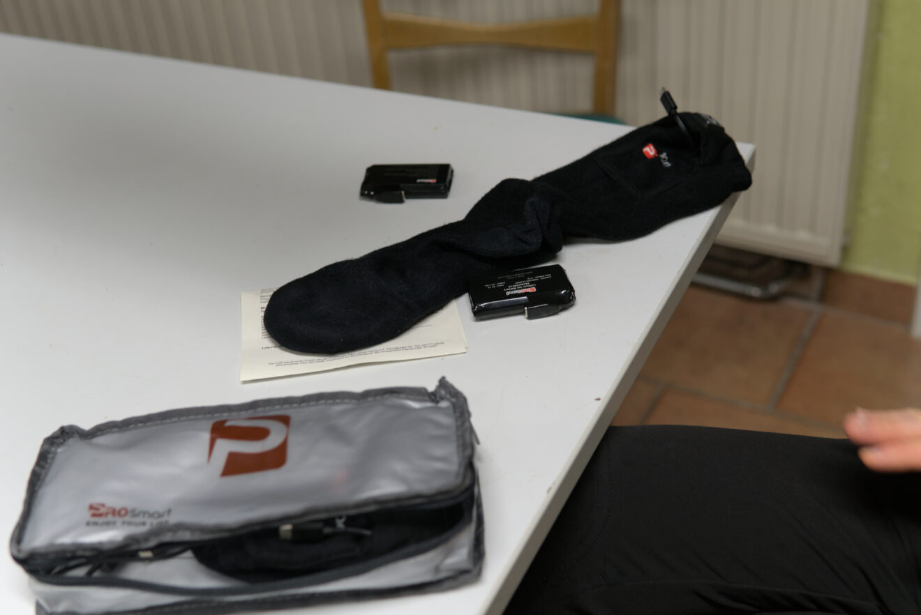 Auf einem Tisch liegt eine schwarze Socke. Daneben ist eine Tasche mit dem dazugehörigen Akku-Gerät.