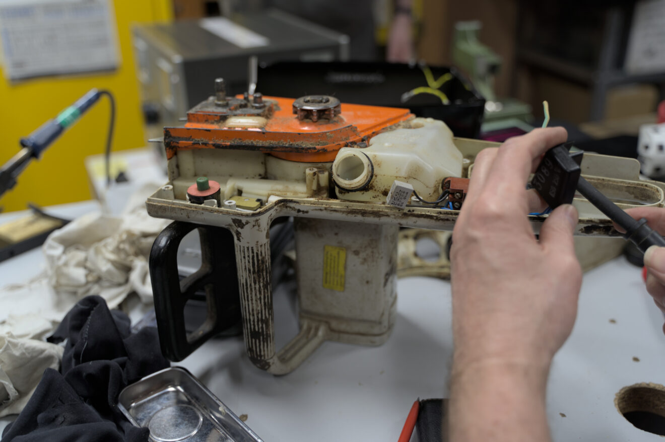 Auf dem Bild ist eine Ketten-Säge der Firma Stihl zu sehen. Das Innere ist aufgeschraubt und ein paar Hände sind zu sehen.