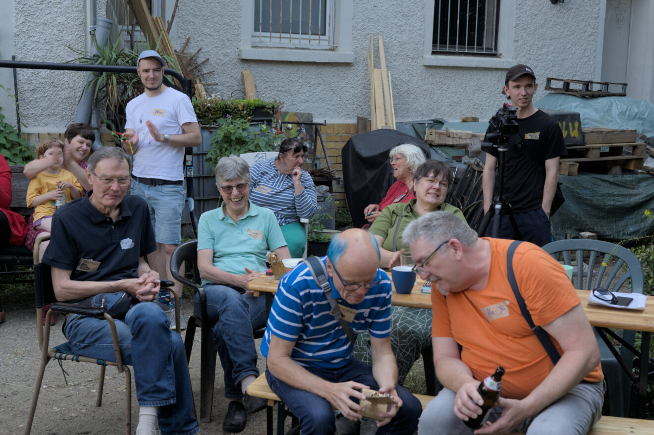 Das Foto zeigt Besucher*innen der Jubiläumsfeier, die am Rand der Bühne sitzen und sich unterhalten oder der Musik lauschen.