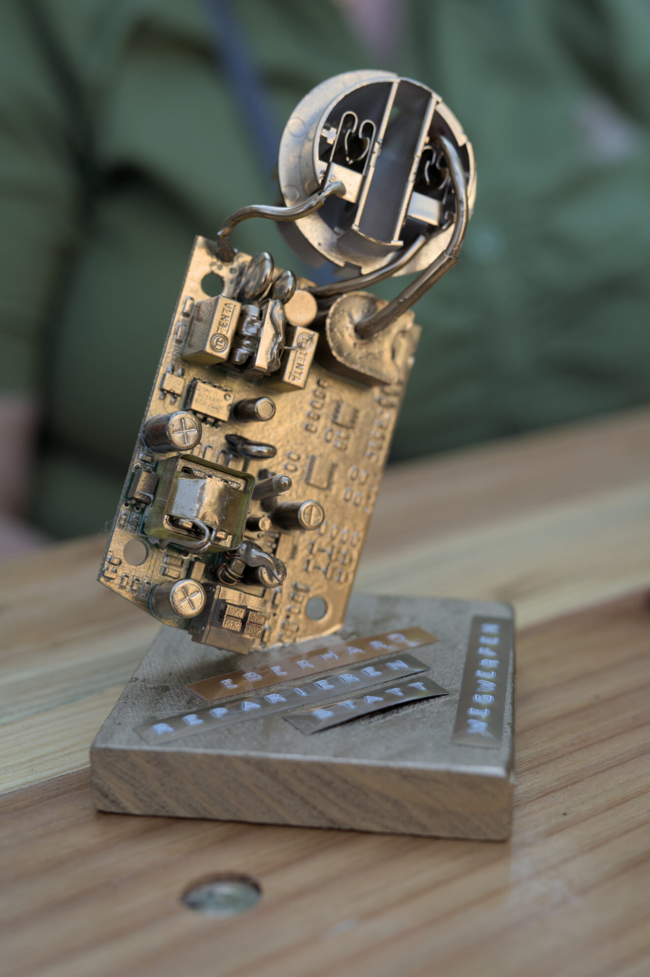 Das Foto zeigt einen goldenen Reparaturpokal aus einer alten Platine auf einem Holz-Sockel