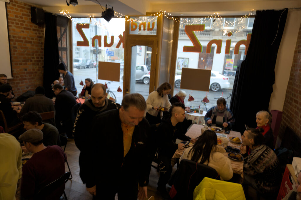 Zu sehen ist ein Eindruck vom Café kaputt Weihnachtsessen: Viele unterschiedliche Menschen sind verteilt an verschiedene kleine Tische im Veranstaltunsraum "hinz und kunz". 